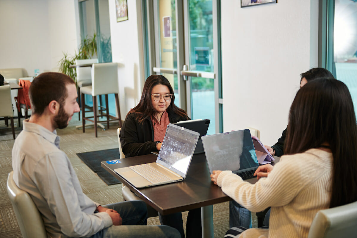 a group of student sitting around a table with laptops.