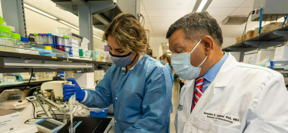 Faculty advising student working with pipette in laboratory