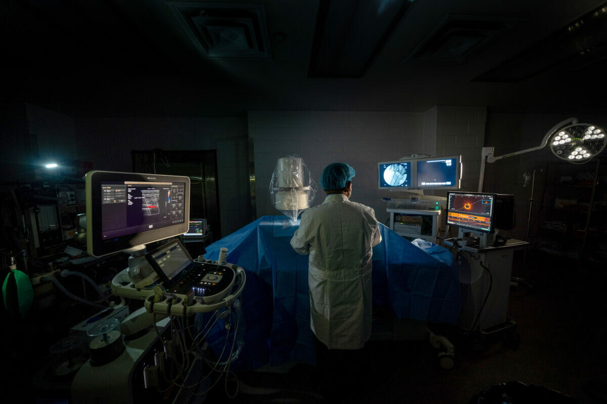 Person in white lab coat working on table with monitors