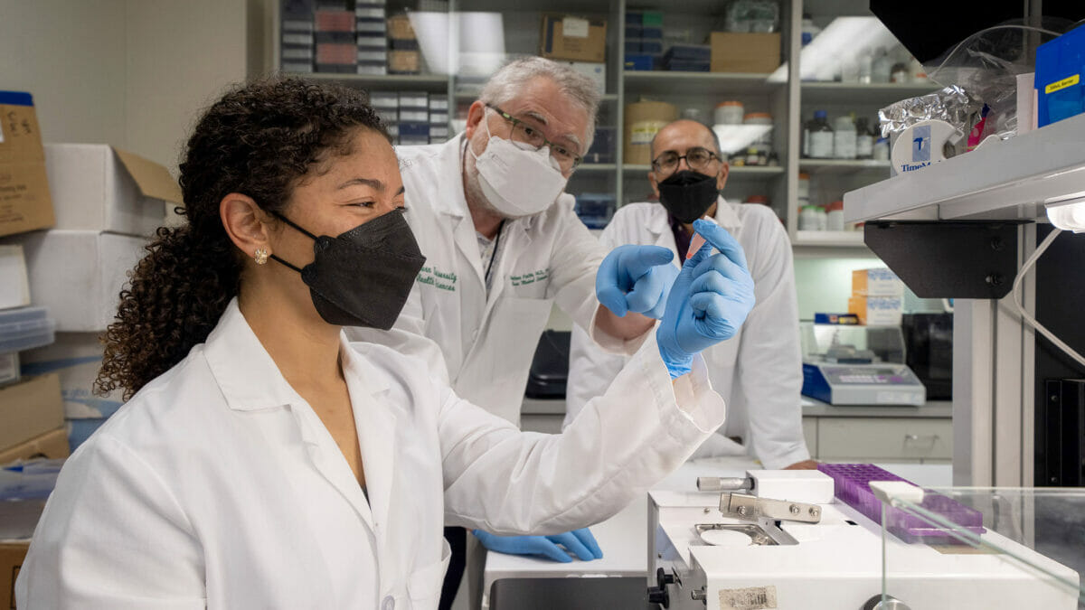 One student and two faculty in white coats observing samples in a lab