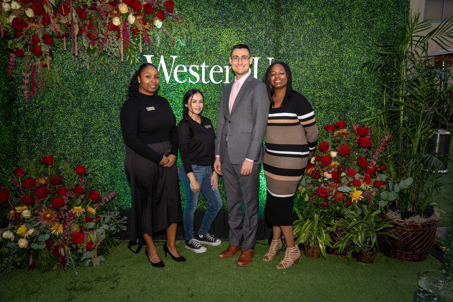 Three females, one male standing, nicely dressed, smiling