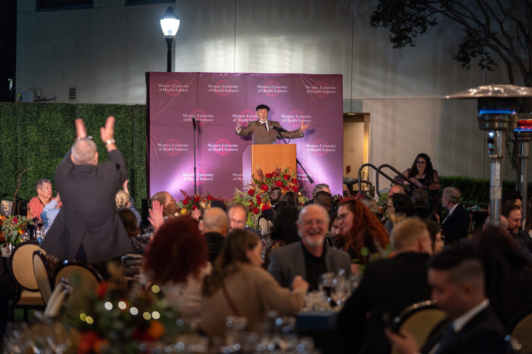 Person at a podium speaking to people sitting at round tables.
