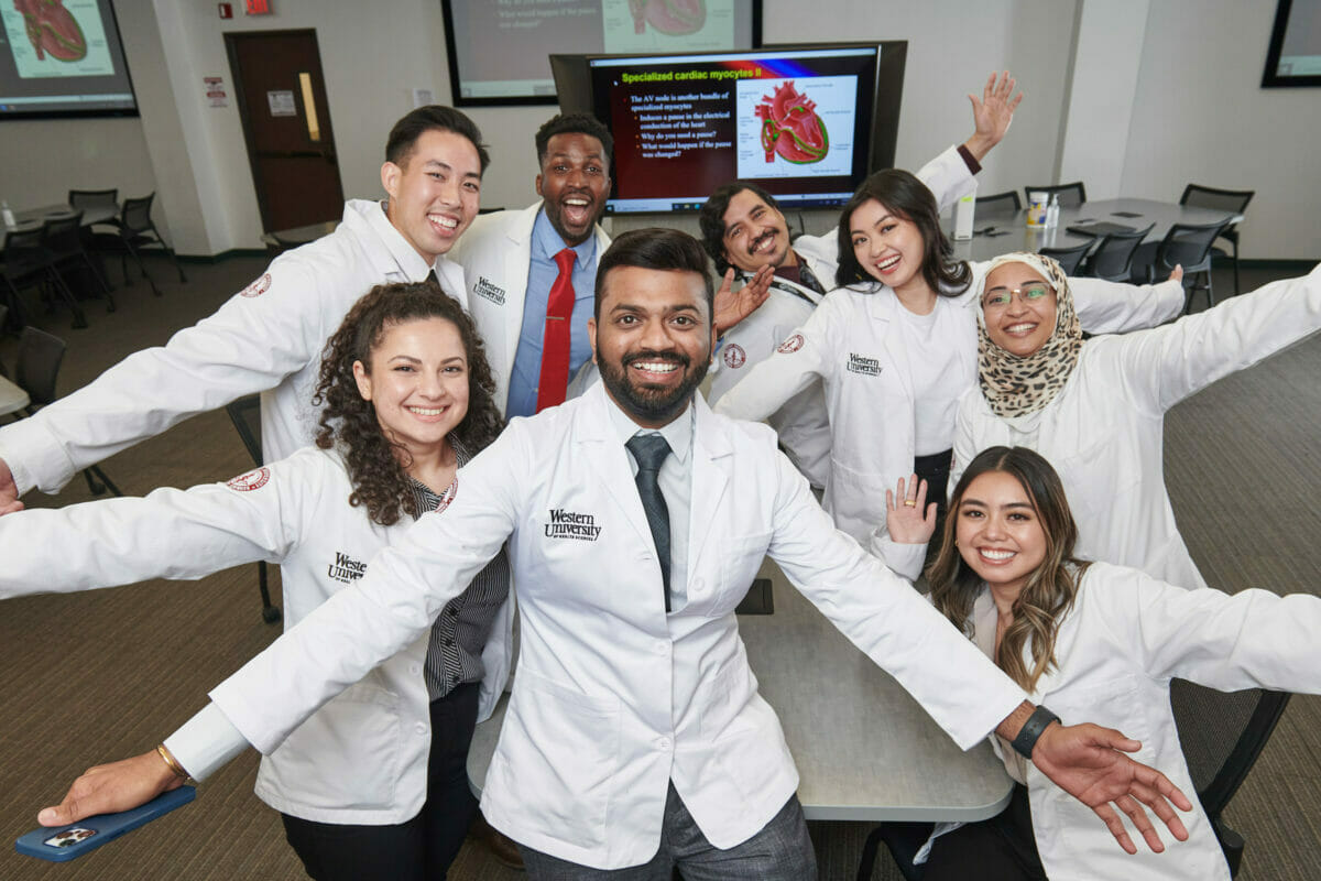 Group, students wearing white coats with outstretched arms.