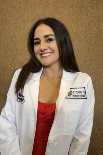 Person smiling, wearing a white lab coat with "OPSO" and "WesternU" logos, over a red top, standing against a beige background.