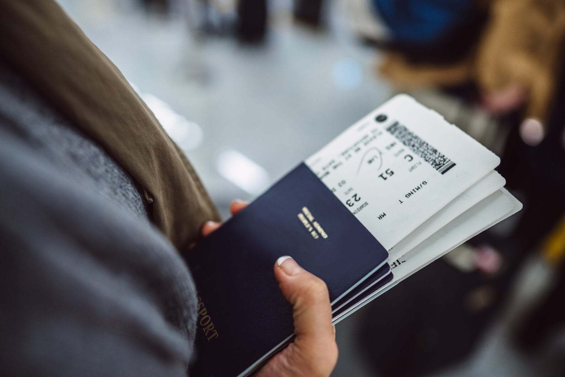A person holds a passport and a boarding pass at an airport, preparing for a flight.
