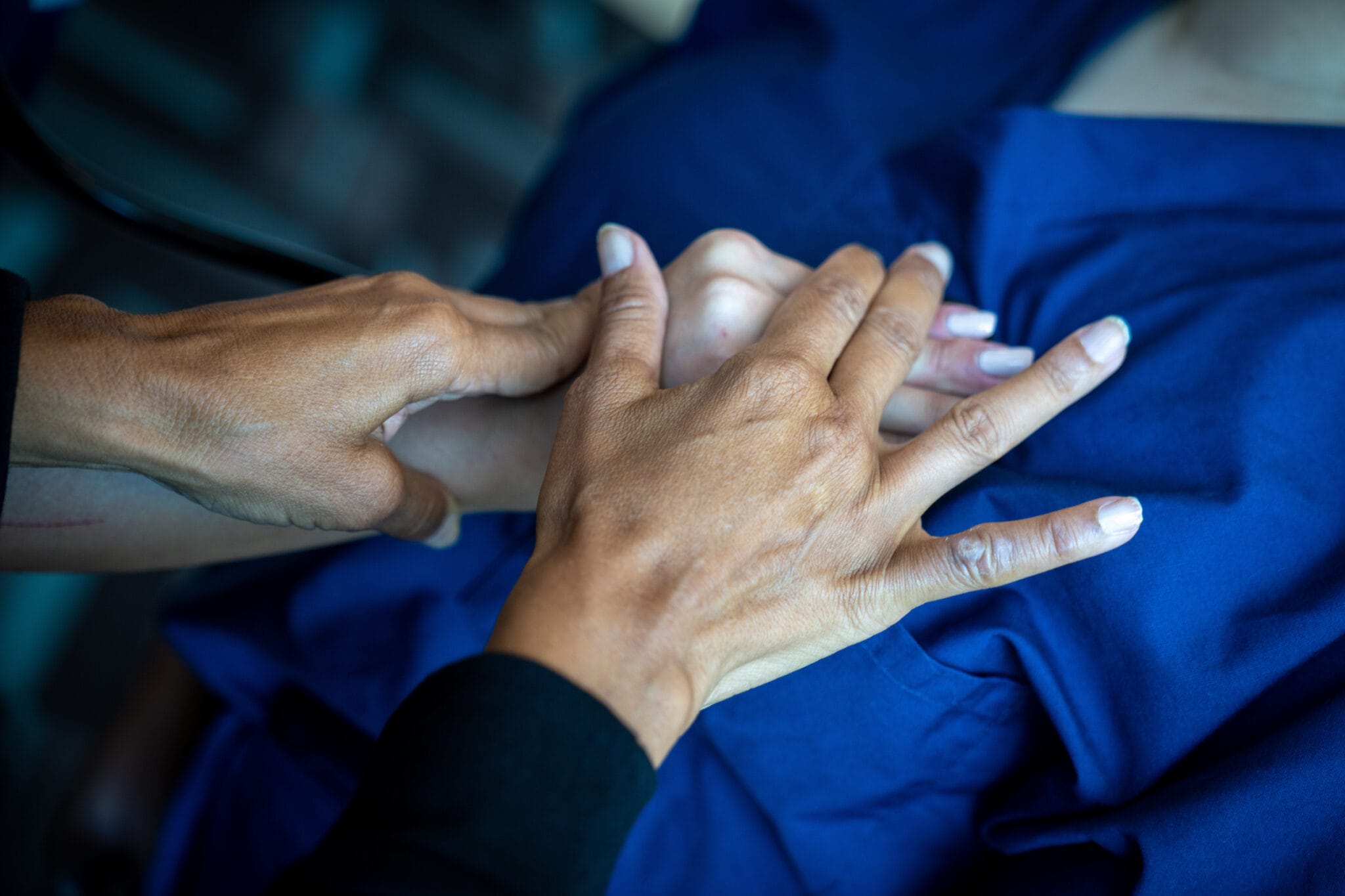 Close-up of a person receiving a hand massage from another individual, both wearing dark blue clothing.
