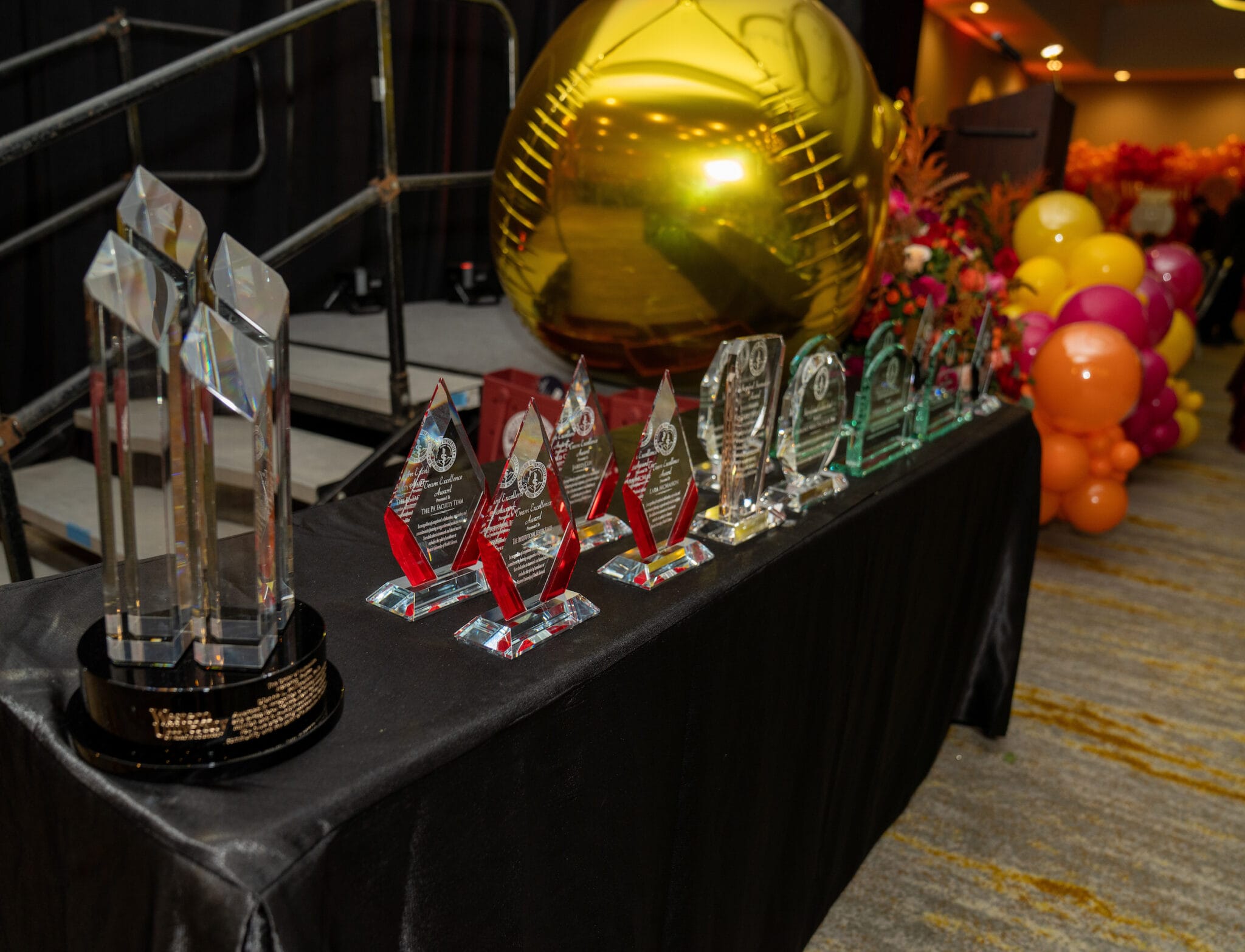A table displays various crystal awards and a large gold football decoration, with colorful balloons and a stage visible in the background.