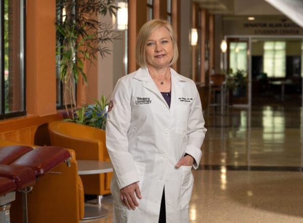 Woman, standing, wearing white doctor coat.