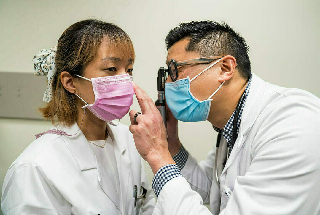 Male nurse looking through device for eye checkup on female student nurse.