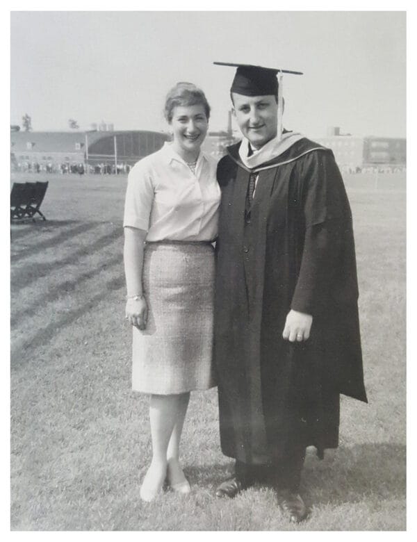 Man in college graduation cap and gown standing next to wife.