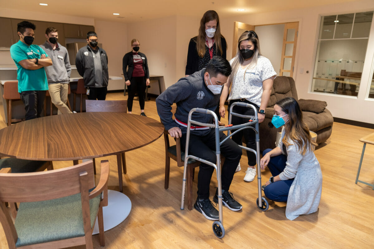 Students providing therapy and training to patient with a walker.